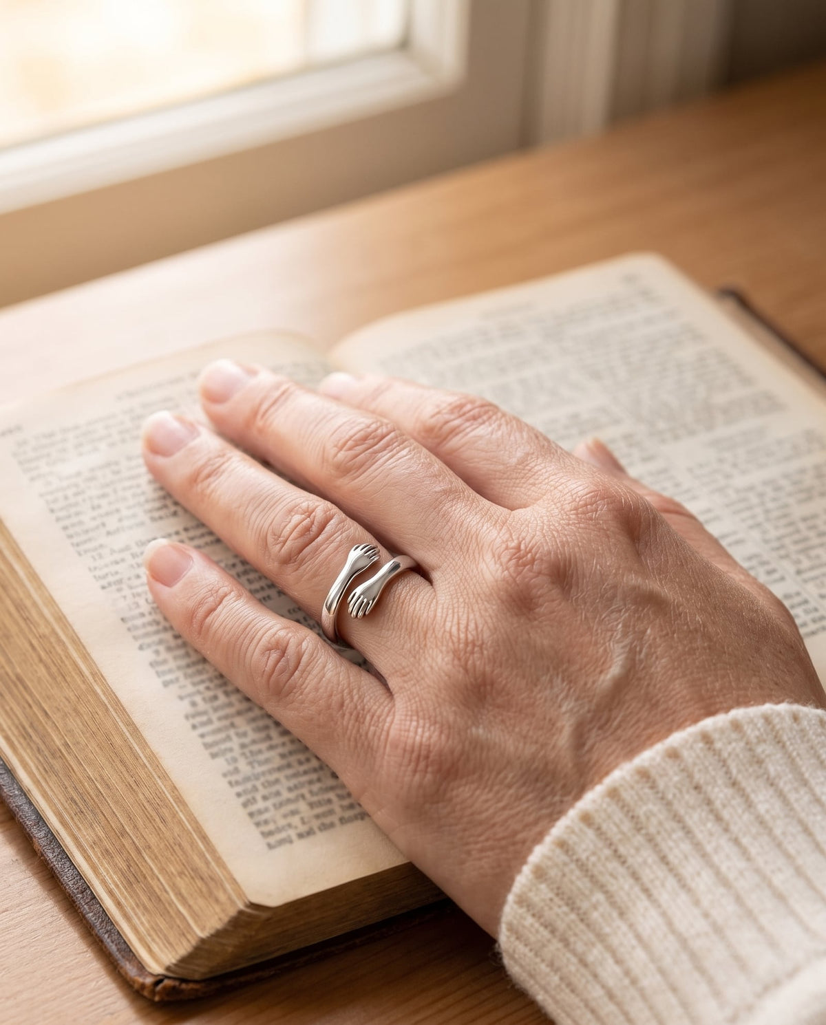 The Everlasting Arms Hug Ring worn on a hand resting on an open Bible